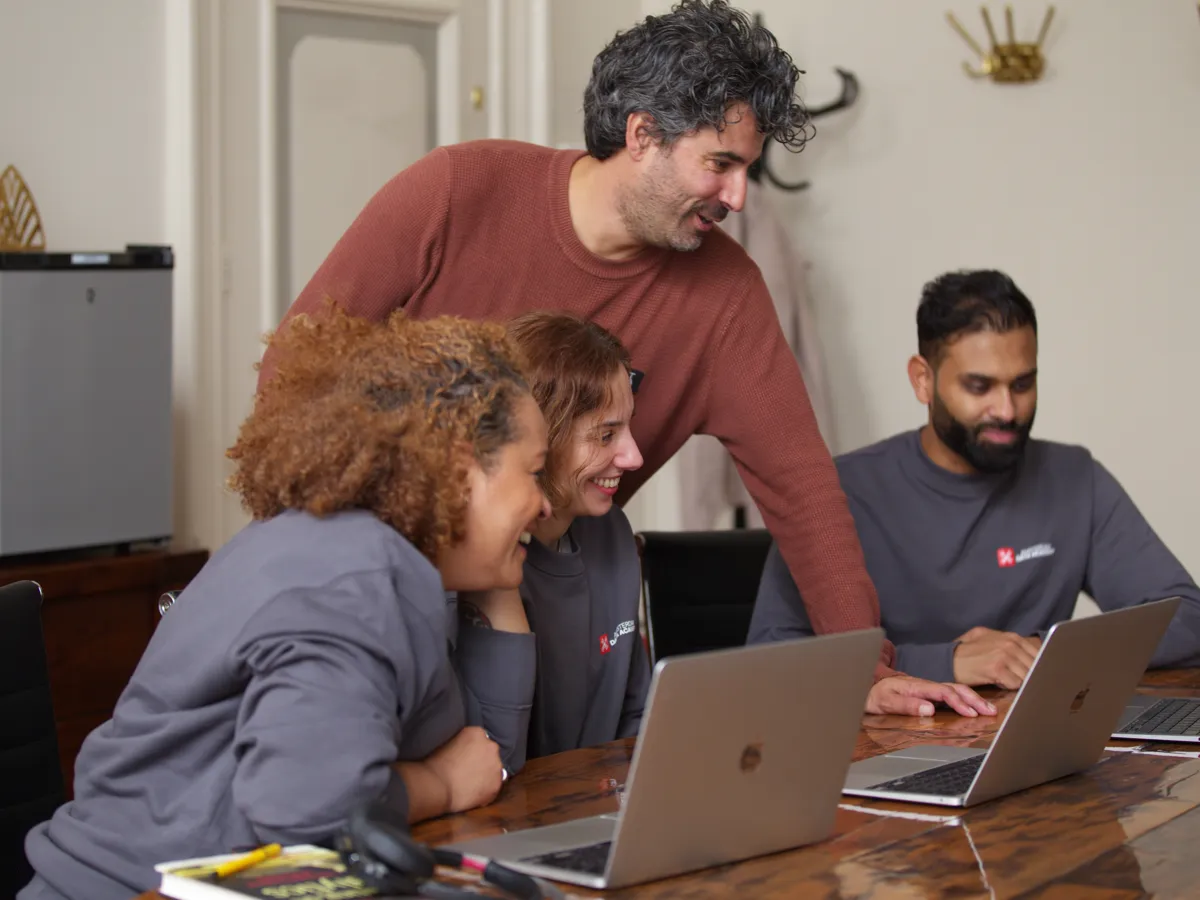 A teacher leans in to help three participants at their laptops
