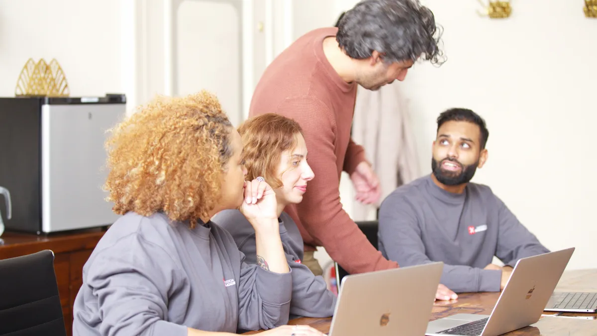 Een docent helpt drie deelnemers achter hun laptop